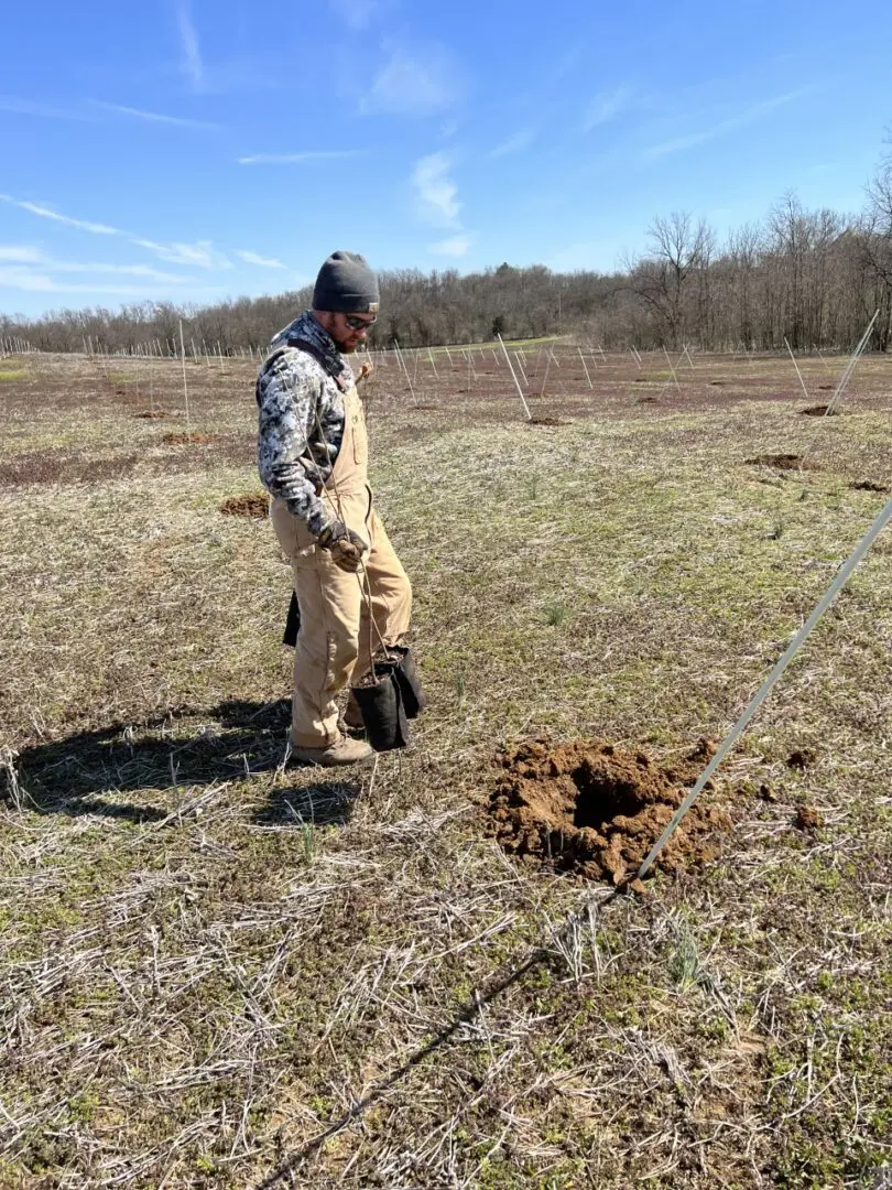 A man in overalls standing next to an ant mound.