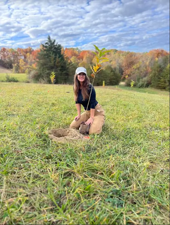 A woman kneeling in the grass with trees behind her.